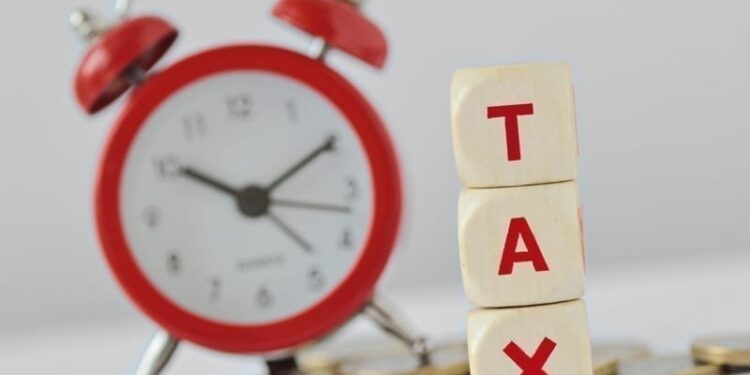 The word Tax written with wooden blocks and alarm clock on coins in the background.