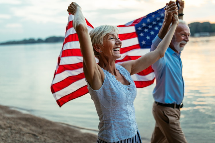 Happy senior men and woman holding an American flag at the beach