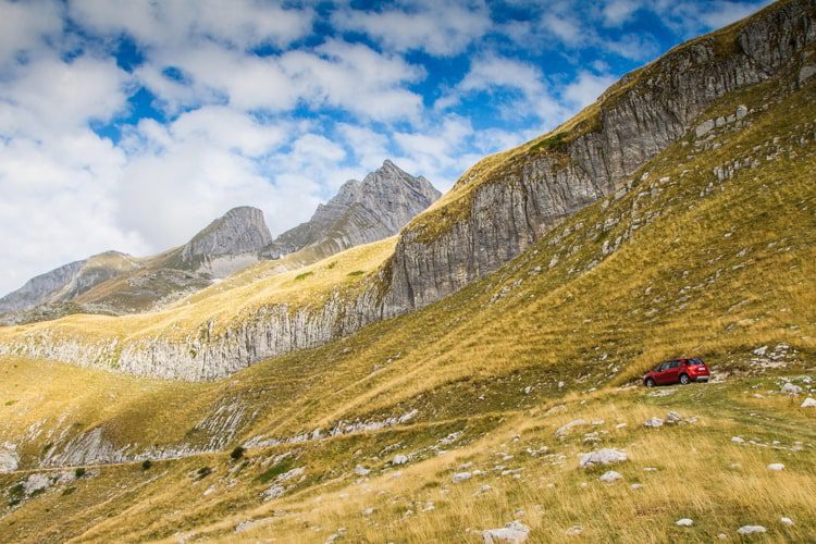 Durmitor National Park in Montenegro with green gras and a red car