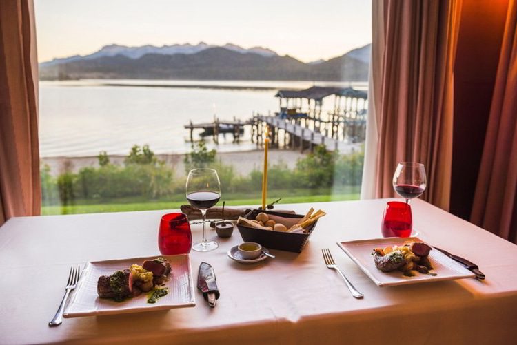 Table set up for dinner at a fine dining restaurant with a glass of red wine, delicious Argentinian steak and beautiful views of lakes and mountains, Patagonia, Argentina