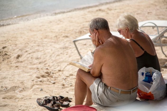 Retired couple sitting on a beach reading a book