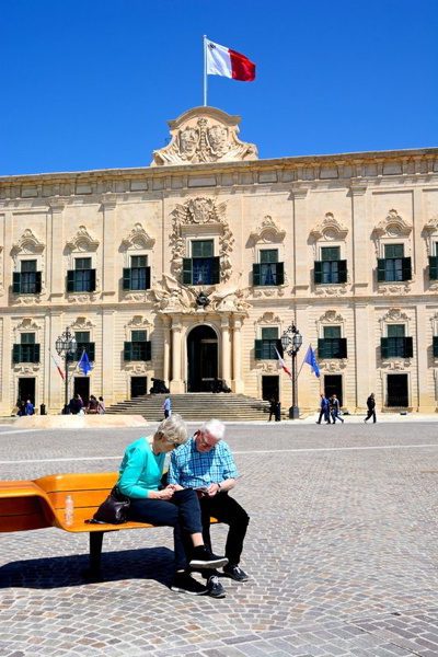 View of the Auberge de Castille in Castille Square with a couple sitting on a bench in the foreground, Valletta, Malta