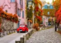 Charming cobblestone street in Montmartre, Paris, with autumn leaves and a classic red car.