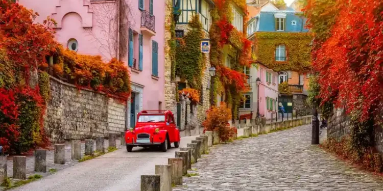 Charming cobblestone street in Montmartre, Paris, with autumn leaves and a classic red car.