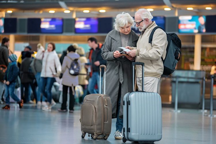 Seniors standing with suitcases at international airport and looking at flight tickets