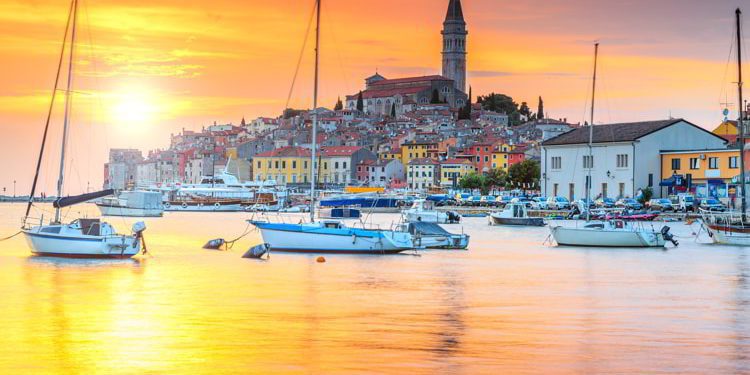 Beautiful sunset in Rovinj harbor in Istria, Croatia, with boats and historical buildings on the background. travel europe on a budget