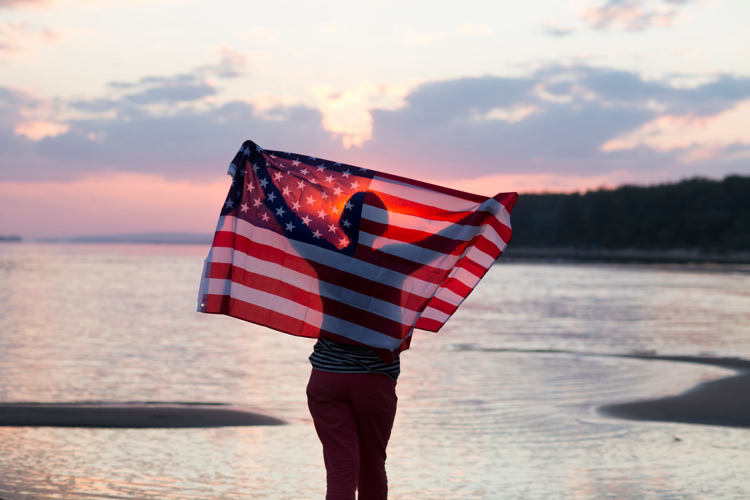 A woman with an American flag at the beach at sunset