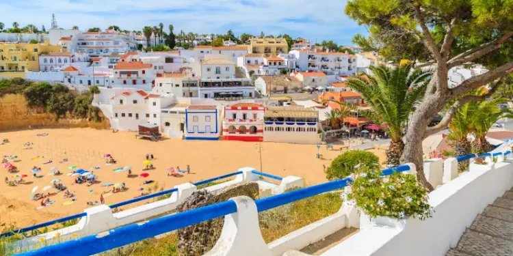 Promenade along street in Carvoeiro fishing village with view of colourful houses on beach, Algarve, Portugal