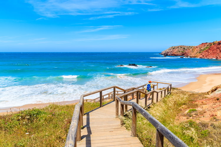 Woman tourist walking to Amado beach on wooden walkway, Algarve, retire in Portugal