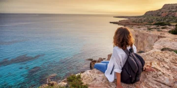 Woman traveler watches a beautiful sunset on the rocks on the beach, Cyprus, Cape Greco