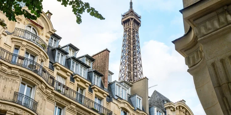 Top of the Eiffel Tower seen from down the street with foliage and typical residential buildings in the foreground. asset protection