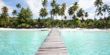 Beach with turquoise water, wooden pier and tropical palm trees, in Thailand,