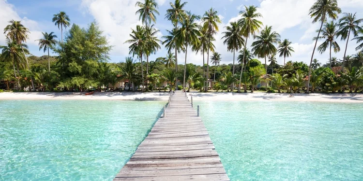 Beach with turquoise water, wooden pier and tropical palm trees, in Thailand,