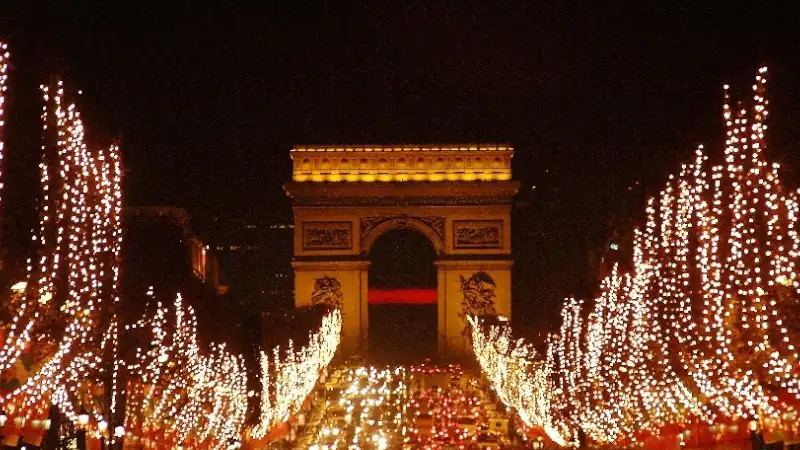 Arc de Triomphe glowing at night with the Champs-Élysées lined in bright, festive holiday lights.