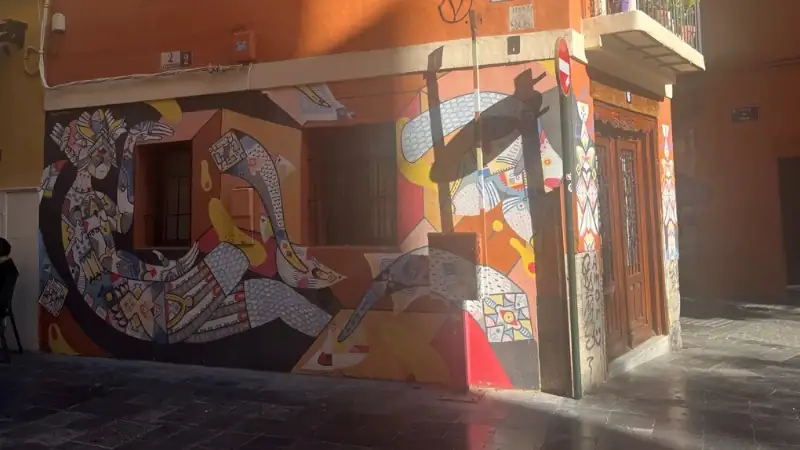 Colorful street art mural on a corner building in Valencia's El Carmen neighborhood, featuring abstract human figures.