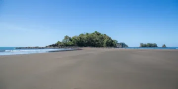 tidal island connected to the mainland by a wide, flat area of sand, likely exposed during low tide