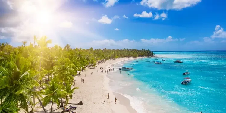 People enjoying a tropical Caribbean beach with white sands and clear waters. Cheapest Places To Live In The Caribbean