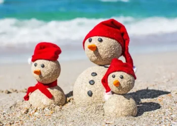 Snowmen family at sea beach in santa hats.