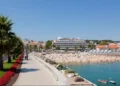 Beachfront promenade in Cascais, Portugal, with palm trees, people on the sandy beach, and calm blue water under a clear sky