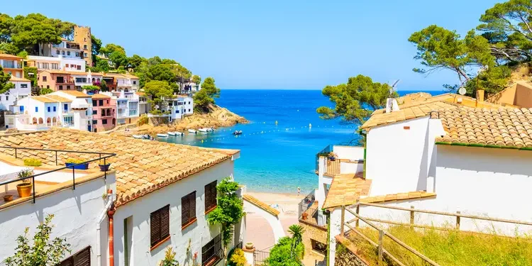 White houses with orange tile roofs and steps to beach in Sa Tuna coastal fishing village, Costa Brava, Spain
