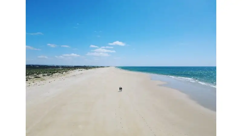 A wide, empty sandy beach stretches into the distance, with the ocean on the right and dunes or vegetation on the left.