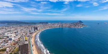 An aerial view of Mazatlán Beach on a sunny morning, showcasing the blue ocean's gentle waves meeting the sandy shores of this popular tourist destination