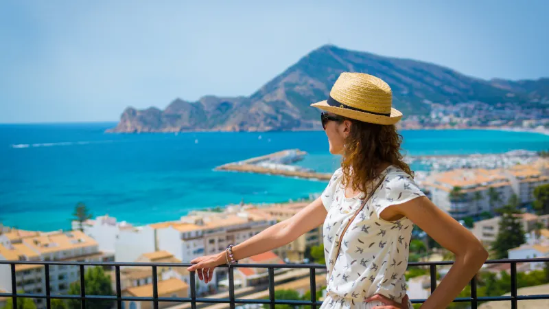woman with straw sunhat looking to the mediterranean sea and enjoying the blue and scenic seascape in Altea, Alicante, Spain
