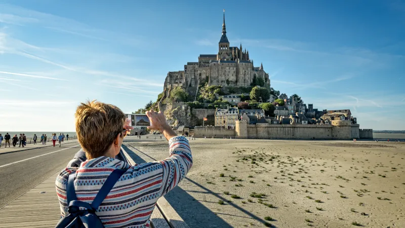 A tourist takes photos of Mont Saint Michel with her smartphone