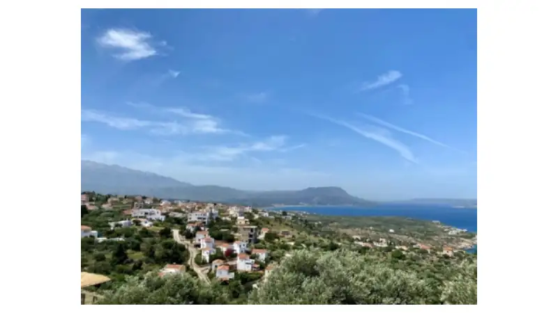 White and pastel houses with red-tiled roofs are scattered along winding roads, surrounded by olive trees and vegetation.