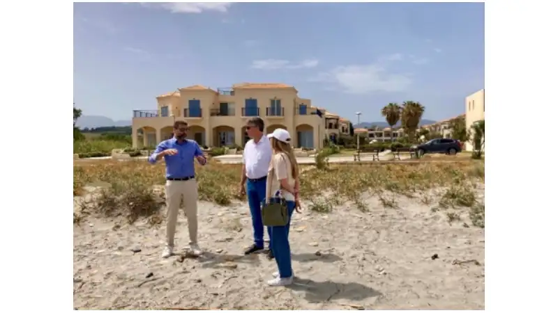 Sophia and Lief are standing on a sandy beachfront lot with a third man who appears to be explaining something, gesturing with his hands as he speaks.