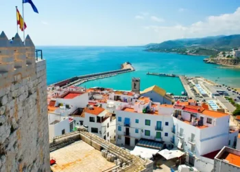 Valencian coastal town in Spain with white buildings, red roofs, and a harbor by turquoise sea.