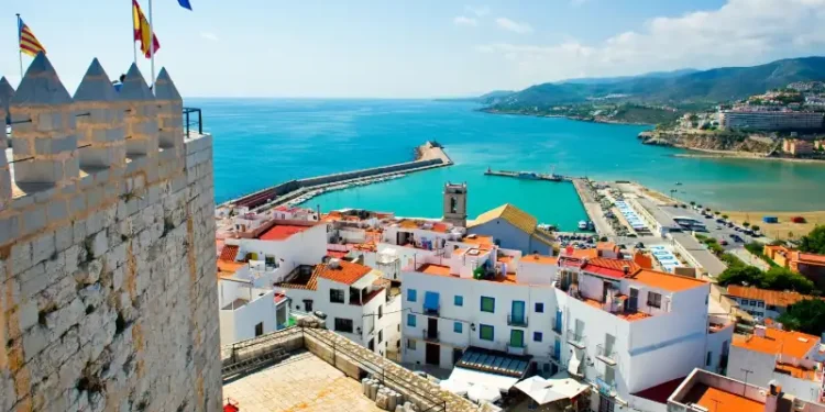 Valencian coastal town in Spain with white buildings, red roofs, and a harbor by turquoise sea.