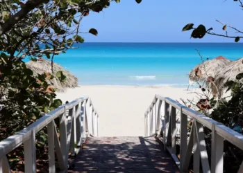 Wooden path to tropical beach with white sand. Picturesque view through green plants to ocean coast, tourist resort on sunny island