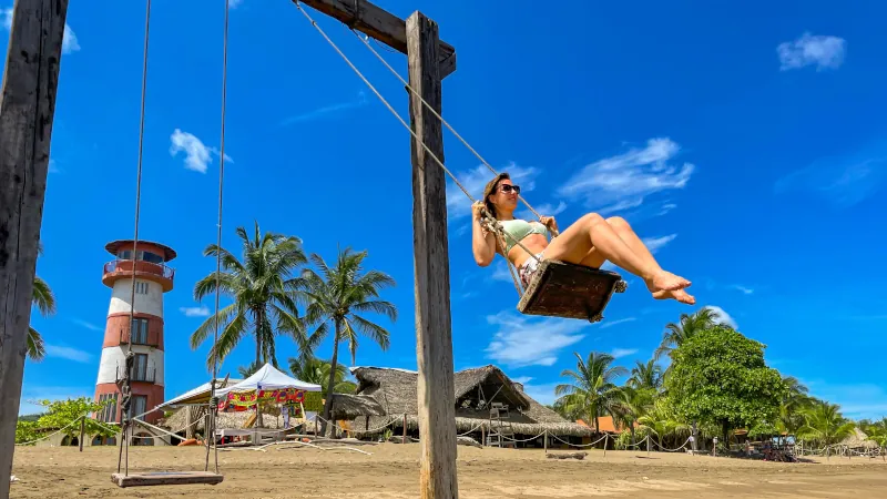 Cheerful tourist enjoying a beach swing in Pedasí with lighthouse in background, representing the joy of living in Panama