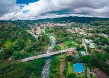 Aerial view of Boquete, Panama, with a river, bridge, and green hills under a cloudy sky.