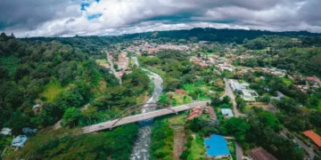 Aerial view of Boquete, Panama, with a river, bridge, and green hills under a cloudy sky.