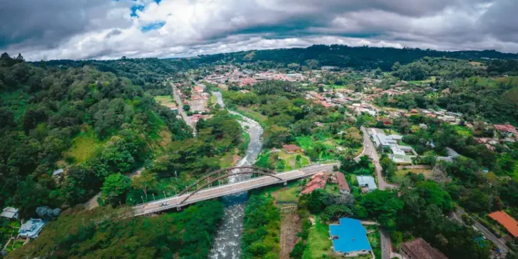 Aerial view of Boquete, Panama, with a river, bridge, and green hills under a cloudy sky.
