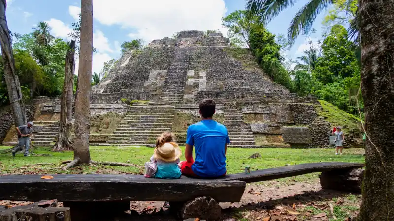 A man and a child looking a pyramid in Belize, surrounded by jungle