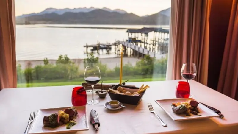 Table set up for dinner at a fine dining restaurant with a glass of red wine, delicious Argentinian steak and beautiful views of lakes and mountains, Patagonia, Argentina