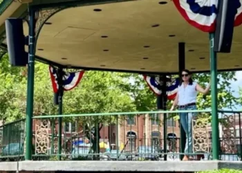A decorated bandstand in Woodstock Town Square with patriotic bunting, surrounded by trees and historic brick buildings on a sunny day.
