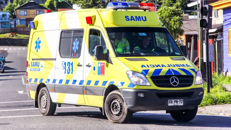 Yellow SAMU ambulance driving on a street in Chile with emergency lights and medical staff inside.