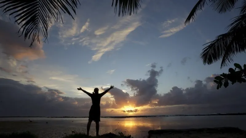 A silhouette of a woman holding her arms out while facing a beautiful sunset.