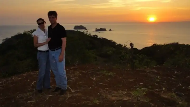 kathleen and lief overlooking the ocean as the sun sets over a tropical coastline.