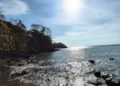 Rocky shoreline with trees overlooking the Pacific Ocean at Los Islotes, Panama, under a bright sun and clear sky.
