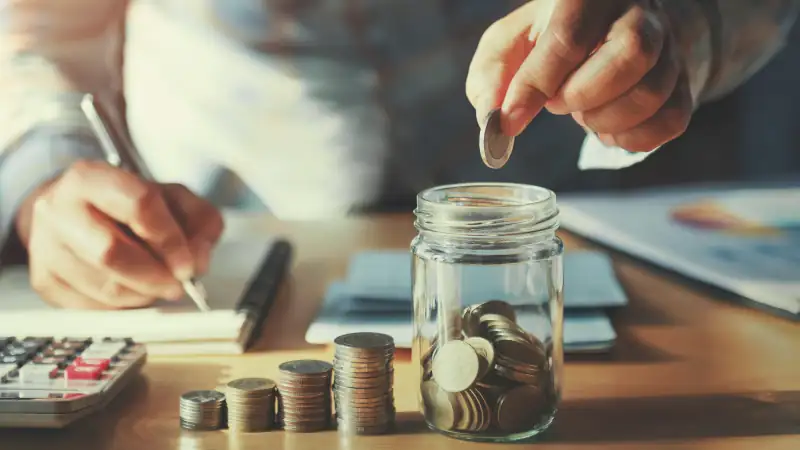 businessman saving money concept. hand holding coins putting in jug glass