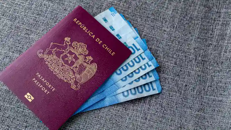 One Red Chilean passport with and some Pesos Chilenos on a gray fabric desk
