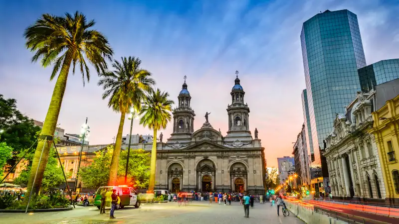 Plaza de Armas in Santiago, Chile, with the cathedral, palm trees, and people at sunset.