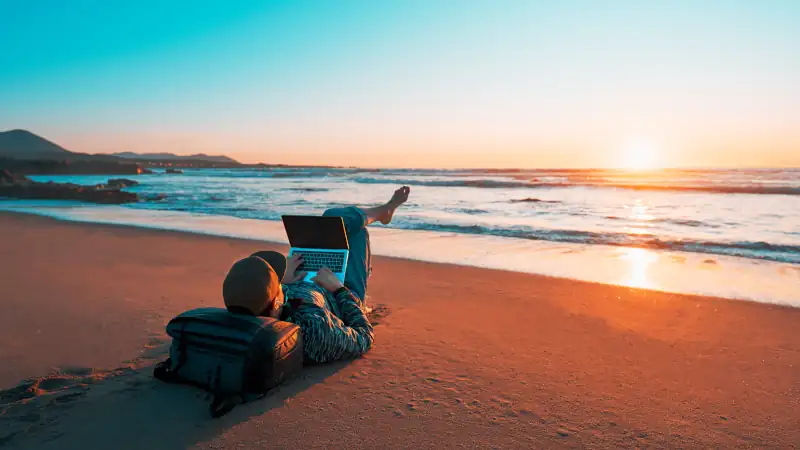 digital nomad laying on the sand of the beach with a laptop working at sunset over the ocean