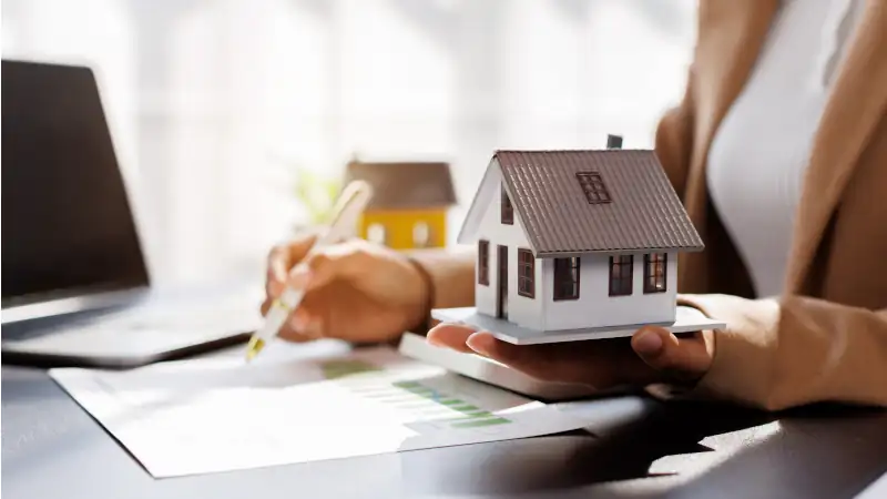 Female woman hand holding home model, investment small miniature white toy house. Mortgage property insurance dream moving home and real estate concept