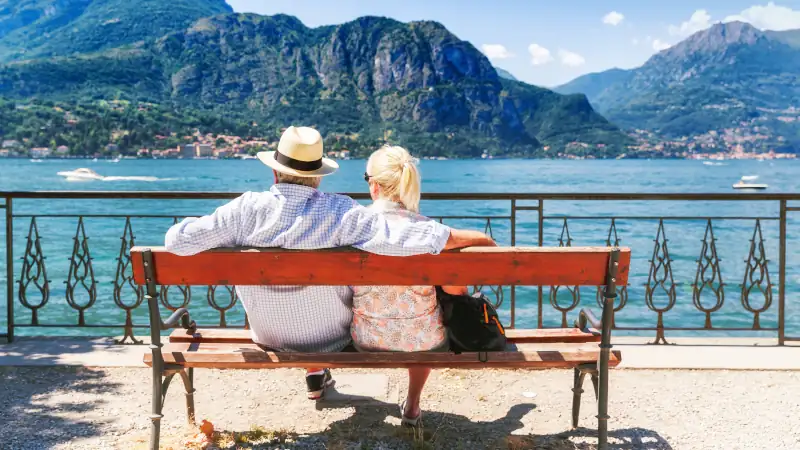 Senior couple weekend getaway having rest on the bench by spectacular lake